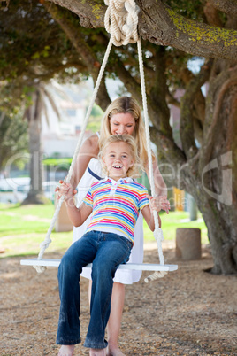 Happy mother pushing her daughter on a swing