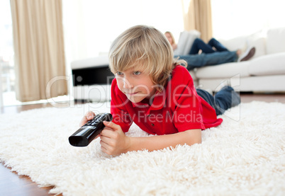 Cute boy holding a remote lying on the floor