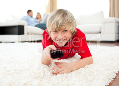 Happy boy holding a remote lying on the floor