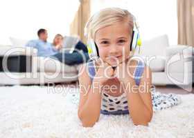 Smiling little girl listening music lying on the floor