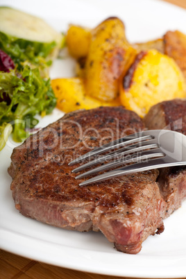 Gabel auf einem Steak mit Salat und Bratkartoffeln