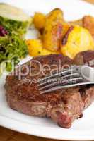 Gabel auf einem Steak mit Salat und Bratkartoffeln
