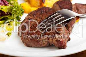 Gabel auf ein Steak mit Salat und Bratkartoffeln