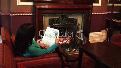 Young woman reading newspaper besides coal fire in luxury hotel 2
