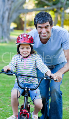 girl learning to ride a bike with her father
