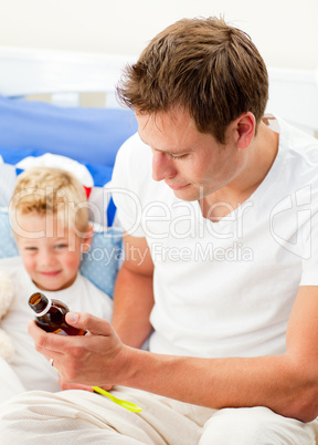 Attractive father giving cough syrup to his sick son