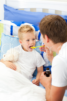 Affectionate father giving cough syrup to his sick son