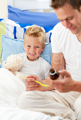 Smiling father giving cough syrup to his sick son