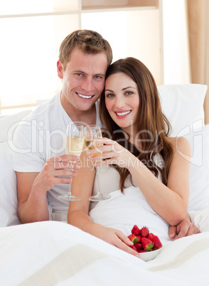 Enamoured couple drinking champagne with strawberries lying in b