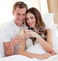 Loving couple drinking champagne lying in bed