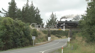 Steam train  and carriages on bridge over a road.
