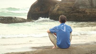 Mann sitzt auf Fels am Meer