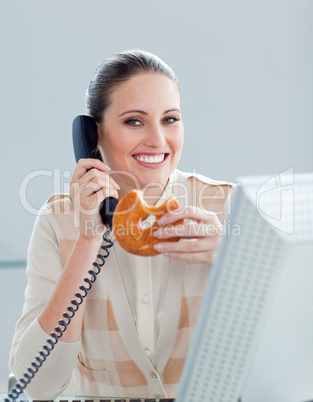 Positive businesswoman on phone eating a donnut