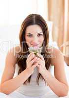 Peaceful woman drinking tea sitting on bed