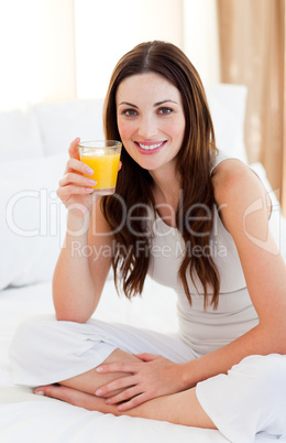 Brunette woman drinking orange juice on bed