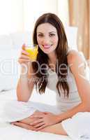 Brunette woman drinking orange juice on bed