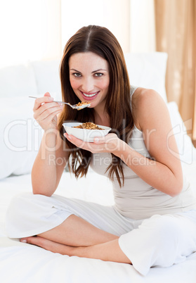 Attractive woman eating cereals sitting on bed