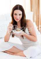 Brunette woman eating cereals sitting on bed