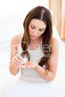 Pensive woman taking a pill sitting on bed