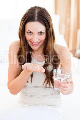 Brunette woman taking a pill sitting on bed