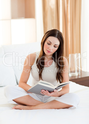 Concentrated woman reading a book sitting on bed