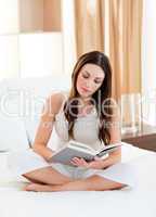 Concentrated woman reading a book sitting on bed