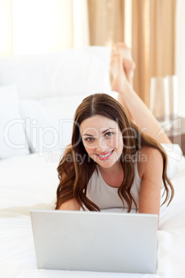 Positive woman looking at a laptop lying on bed