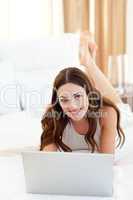 Positive woman looking at a laptop lying on bed