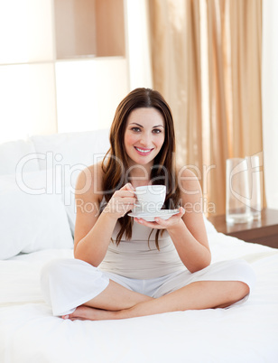 Smiling woman drinking coffee sitting on bed