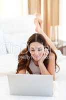 Brunette woman looking at a laptop lying on bed