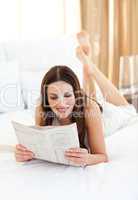 Elegant woman reading newspaper lying on bed
