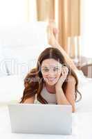 Smiling woman looking at a laptop lying on bed