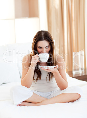 Pretty woman drinking coffee sitting on bed