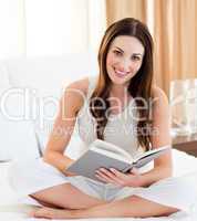 Smiling woman reading a book sitting on bed