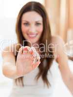 Smiling woman taking a pill sitting on bed