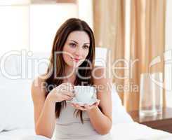 Relaxed woman drinking coffee sitting on bed