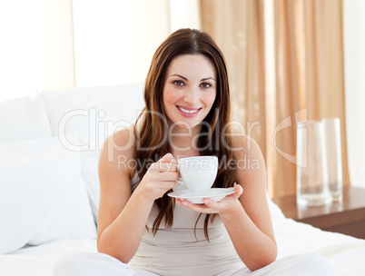 Charming woman drinking coffee sitting on bed