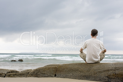 Mann meditiert auf einem Felsen am Meer