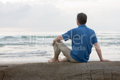 Mann sitzt auf Fels am Strand