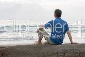 Mann sitzt auf Fels am Strand