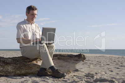 Mann arbeitet mit Laptop am Strand