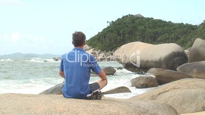 Mann meditiert auf Fels am Meer