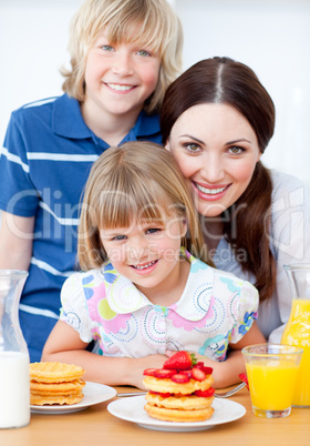 Jolly mother and her children eating waffles with strawberries