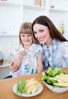 Cheerful little girl eating vegetables with her mother