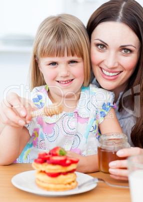 Adorable little girl and her mother putting honey on waffles