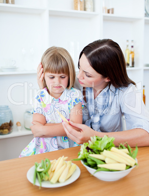 Dissatisfied blond girl eating vegetables with her mother