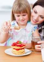 Cute little girl and her mother putting honey on waffles