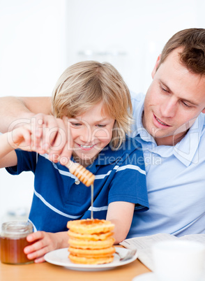 Jolly boy and his father putting honey on waffles