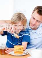 Jolly boy and his father putting honey on waffles