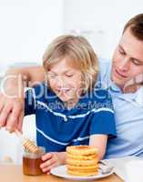 Adorable boy and his father putting honey on waffles